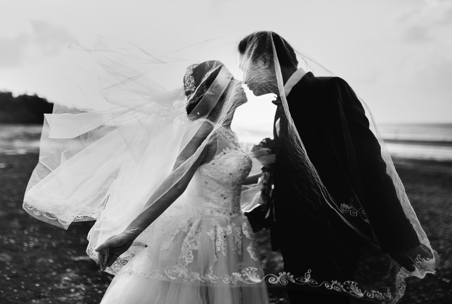 Braut und Bräutigam küssen sich unter einem Schleier in einer romantischen Hochzeitsszene in Schwarz-Weiß