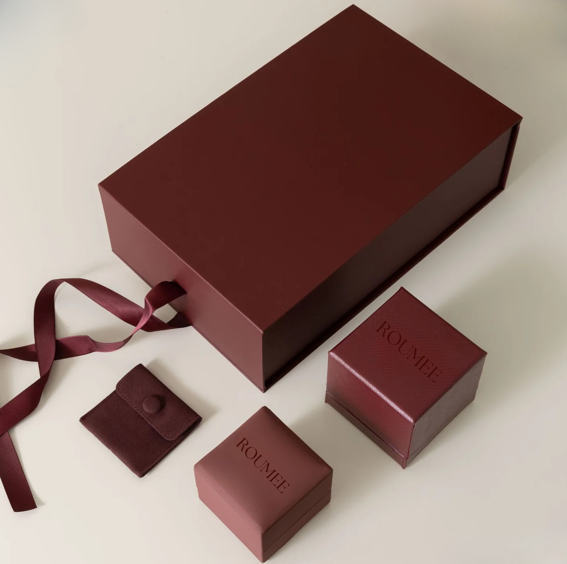 Elegante Schmuckverpackung in Maroon-Farbe mit mehreren Ringboxen und Schleife als Symbol für liebevolle Verpackung und sicheren Versand von Trauringen